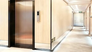 A modern hotel corridor with a wooden wall, a metallic elevator, and a floor with a light-colored carpet. - LinghangHostel (Shenzhen)