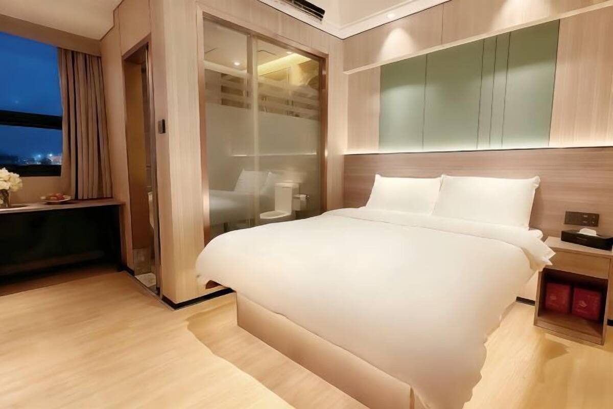 A modern hotel room with a large bed, a desk, and a sliding door leading to a balcony.