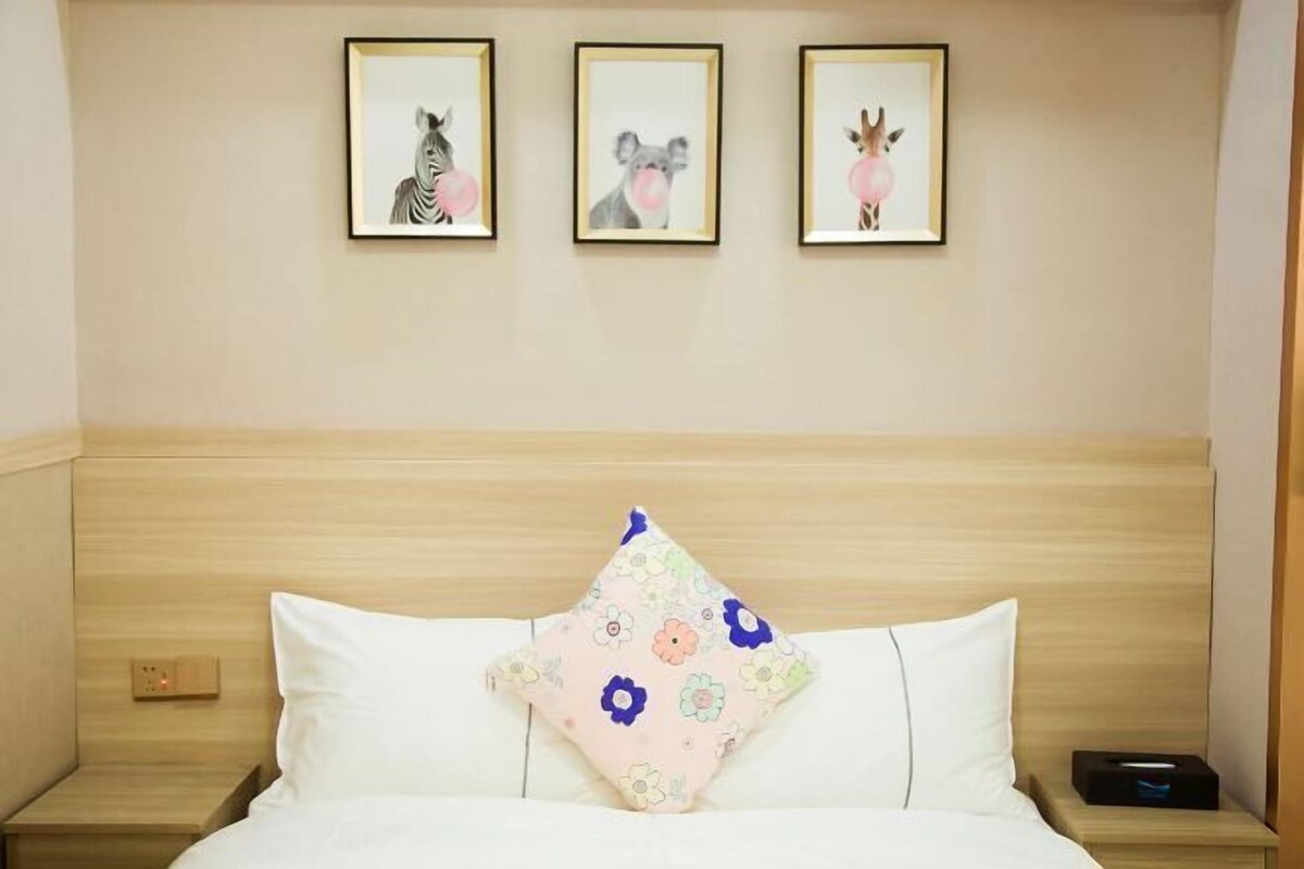 A hotel room with a wooden headboard, a bed with white bedding, a floral pillow, and three framed animal pictures on the wall.