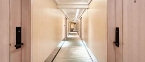 A hotel corridor with doors on both sides, a carpeted floor, and a ceiling with recessed lighting.