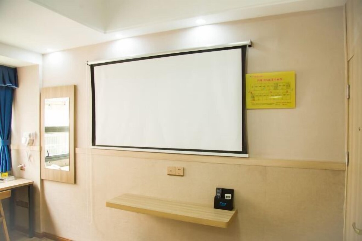 A conference room with a whiteboard, a small shelf with a device, and a yellow sign on the wall.