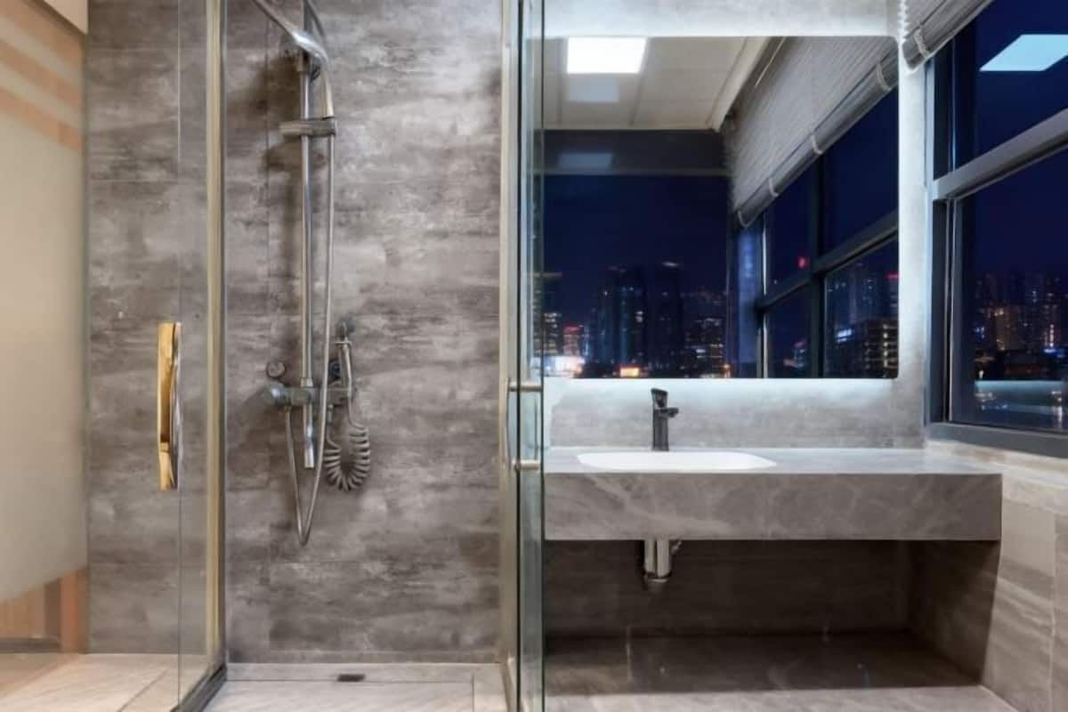 A modern bathroom with a glass shower enclosure, a sink, and a city view.