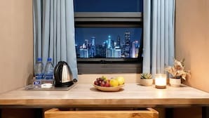 A hotel room with a cityscape view, a wooden table with a kettle, a bowl of fruit, a candle, and a small plant. - LinghangHostel (Shenzhen)