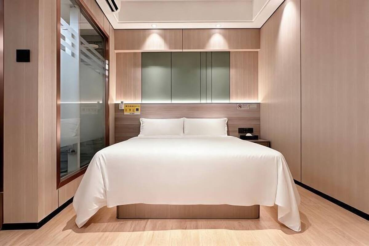 A modern hotel room with a large bed, built-in cabinets, and a glass partition.
