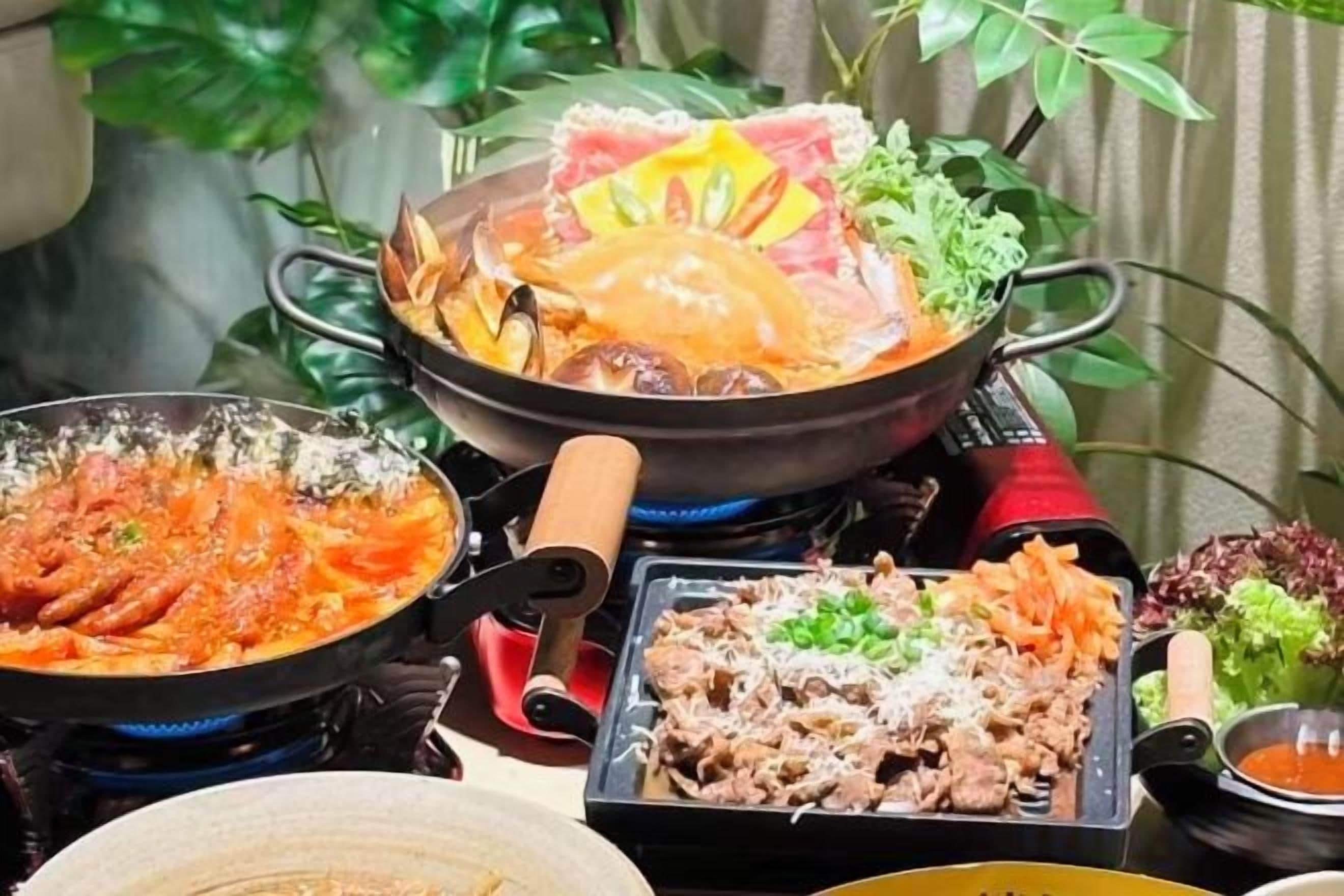 A table with various dishes, including a hot pot, grilled meat, and vegetables.