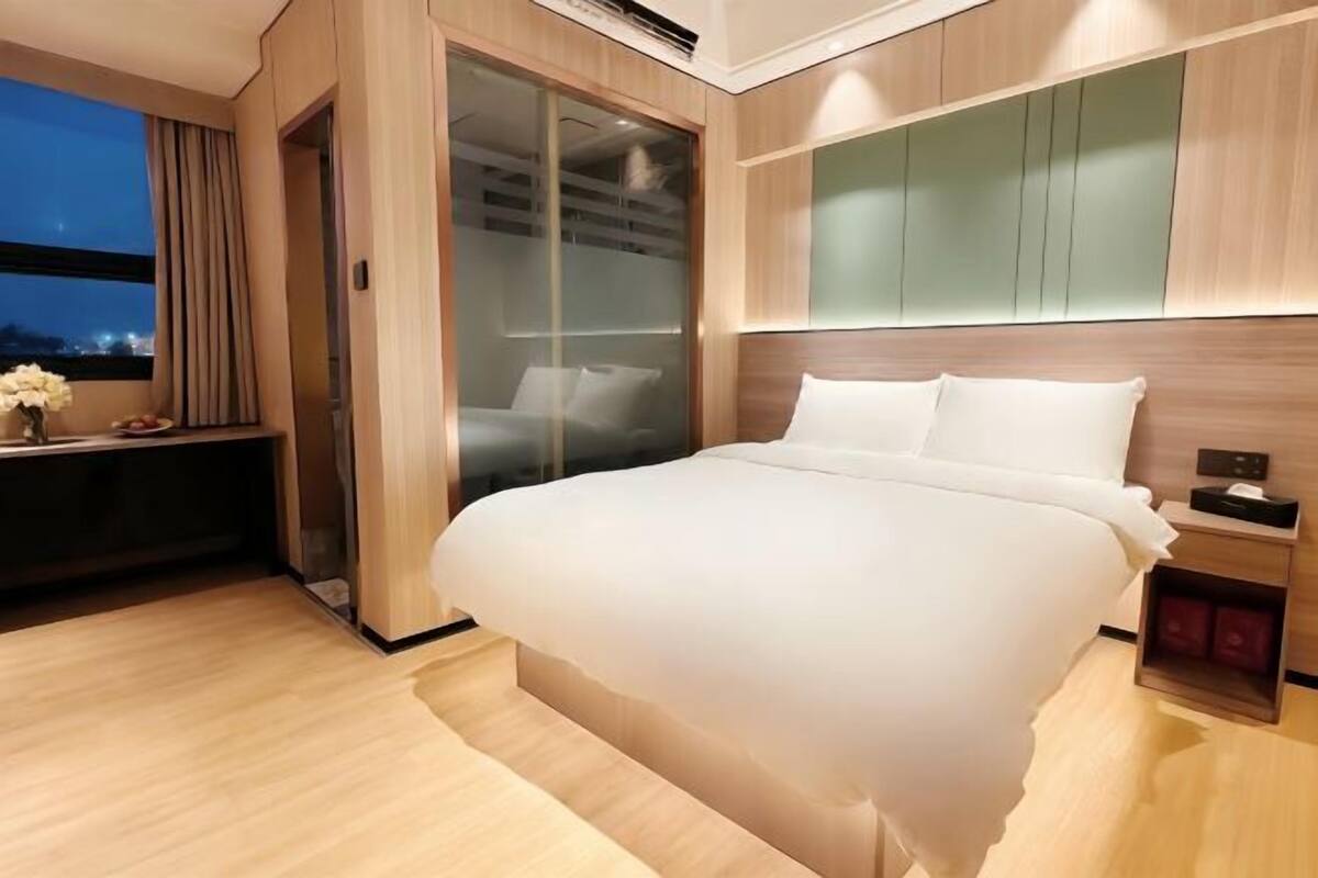 A modern hotel room with a large bed, a desk, and a sliding door closet.