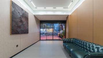 A lobby with a green leather sofa, a large abstract painting, and a view through glass doors to an outdoor area.