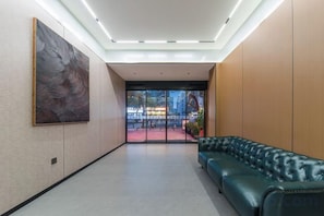 A lobby with a green leather sofa, a large abstract painting, and a view through glass doors to an outdoor area. - ZhenXing hotel (Shenzhen)