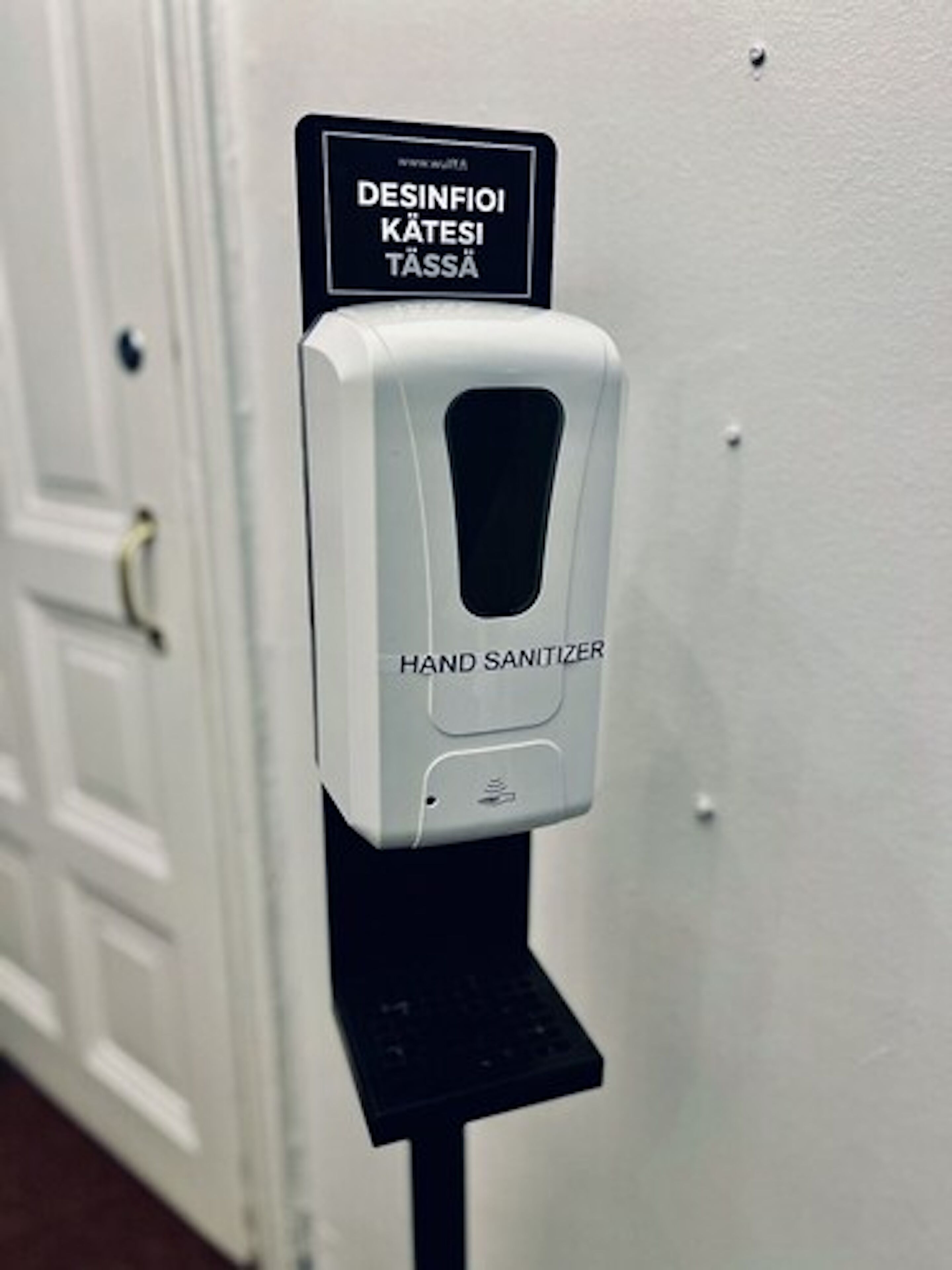 A hand sanitizer dispenser mounted on a wall with a sign above it.