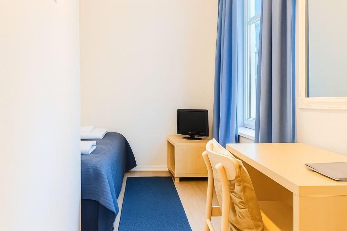 Una habitación de hotel con cama, escritorio, televisor, silla y ventana con cortinas.