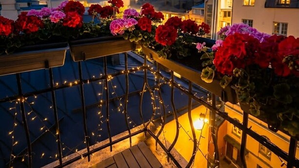 A balcony with flowers and string lights, overlooking a body of water and buildings. - Senate Hotel (Helsinki)