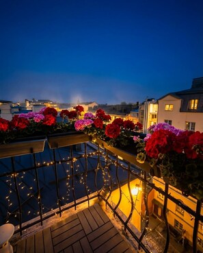 A balcony with flowers and string lights, overlooking a body of water and buildings. - Senate Hotel (Helsinki)