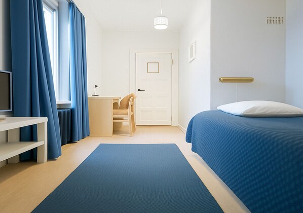 A modern bedroom with a bed, a desk, a chair, and a window with curtains. - Senate Hotel (Helsinki)