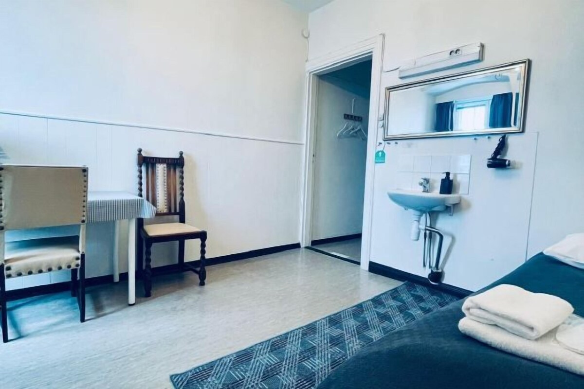 Una habitación de hotel con una cama, una silla, una mesita, un lavamanos y un espejo.