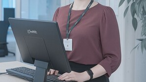 A person standing at a desk with a computer, wearing a lanyard with an ID badge. - Senate Hotel (Helsinki)