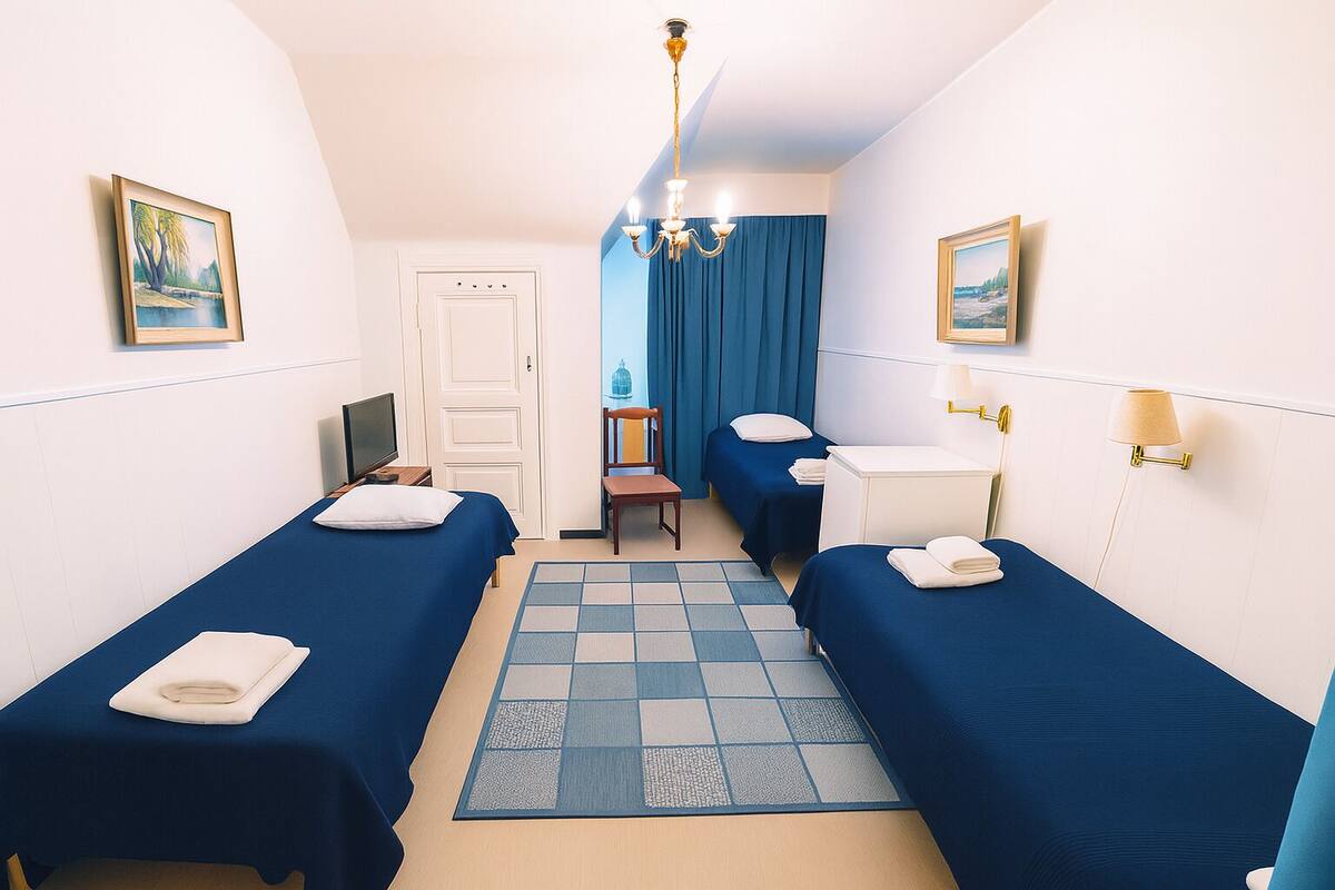 Ein Hotelzimmer mit zwei Einzelbetten, einem Schreibtisch, einem Stuhl, einem Fernseher und Blick auf einen blauen Vorhang.