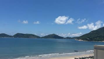 A beach with clear blue water, sandy shore, and distant green hills.
