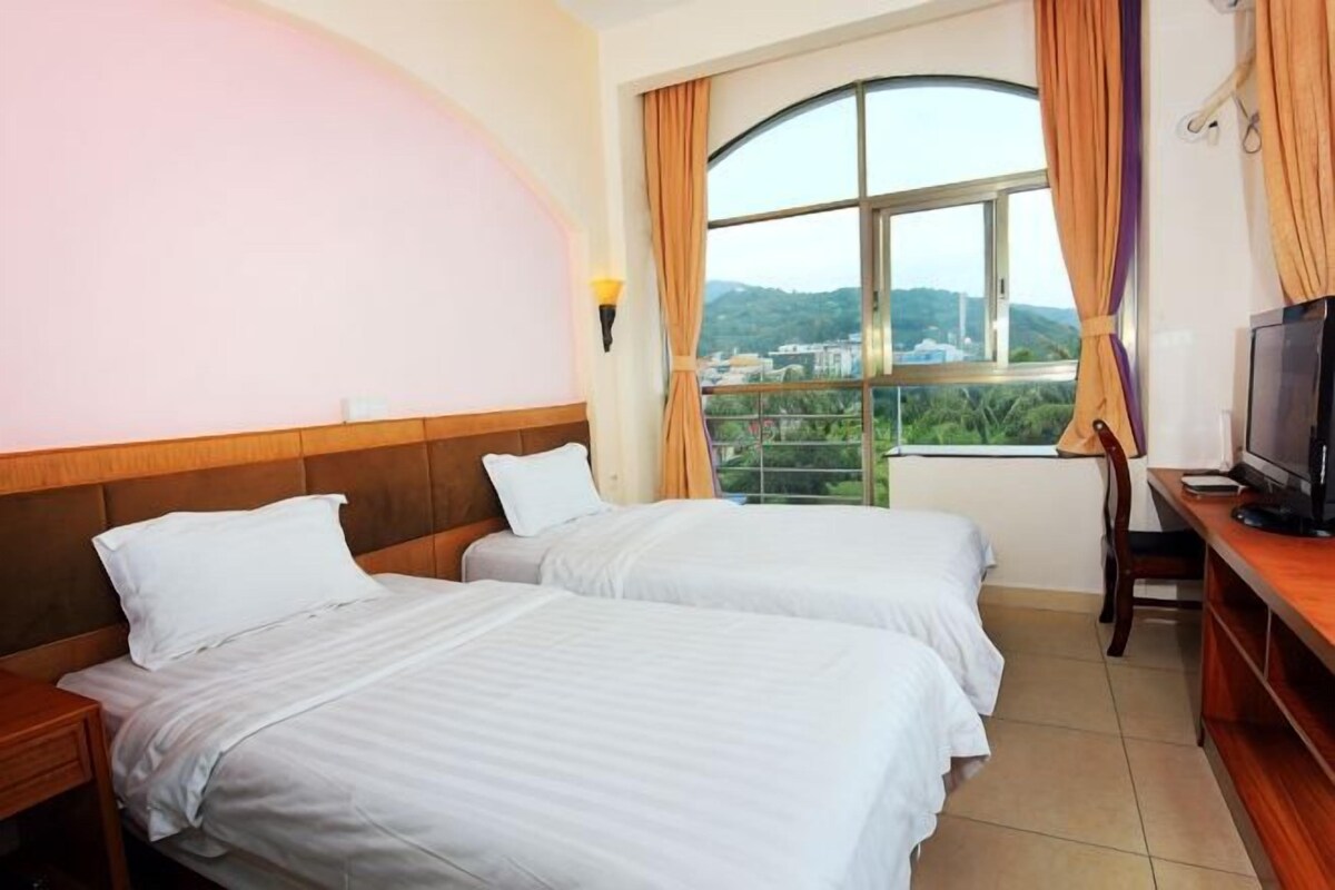 Habitación de hotel con dos camas, televisión, escritorio y ventana con vista a la ciudad.