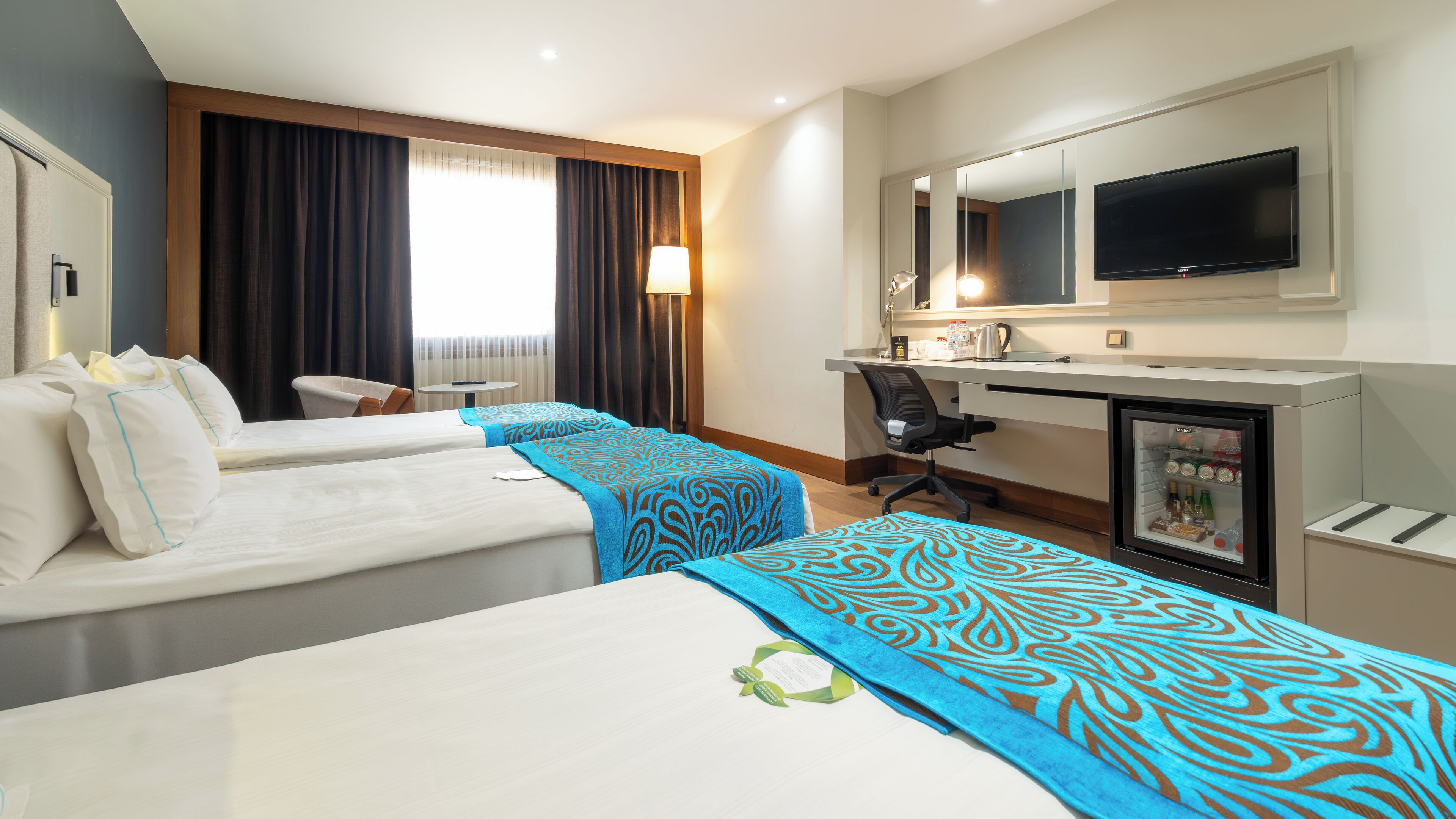 A hotel room with two beds, a desk, a chair, a television, and a minibar.