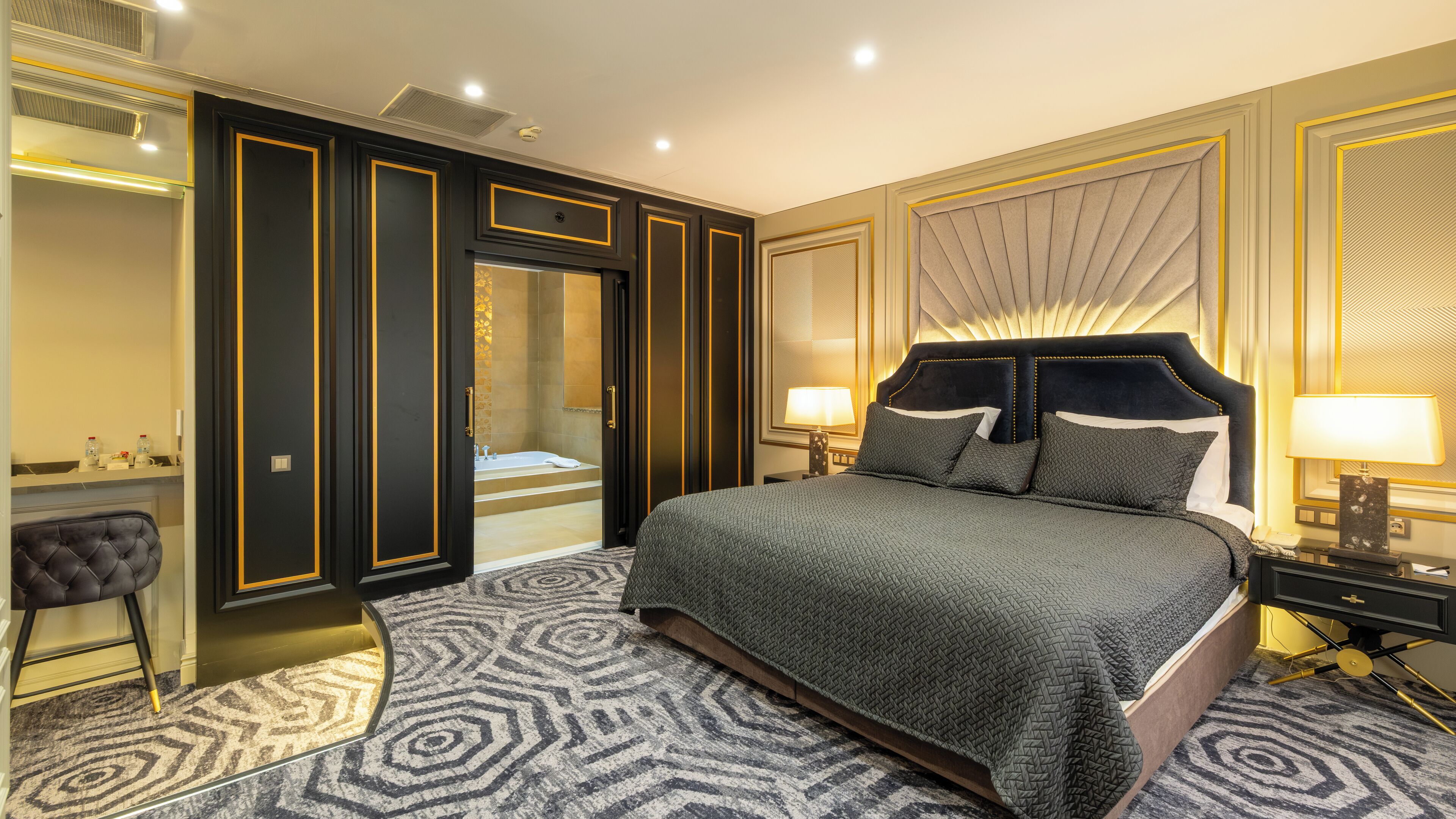 A luxurious bedroom with a large bed, a vanity with a mirror, a chair, and a walk-in closet.