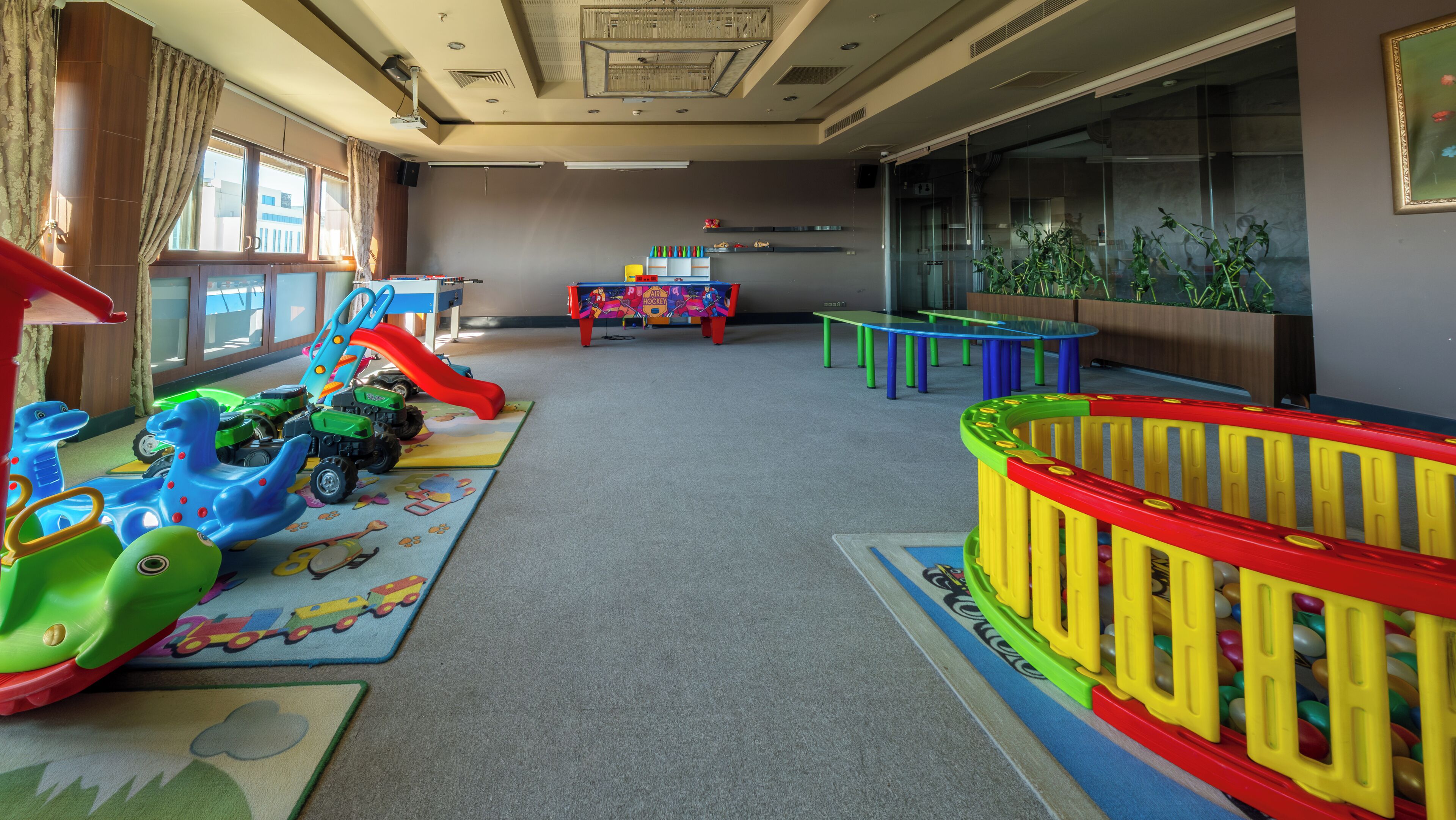 Un área de juegos infantiles con equipo colorido, que incluye un tobogán y coches de juguete, además de una mesa con juguetes.