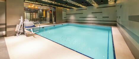 Une grande piscine intérieure au design moderne, comprenant un escalier d’accès et un espace détente avec des chaises et une table.