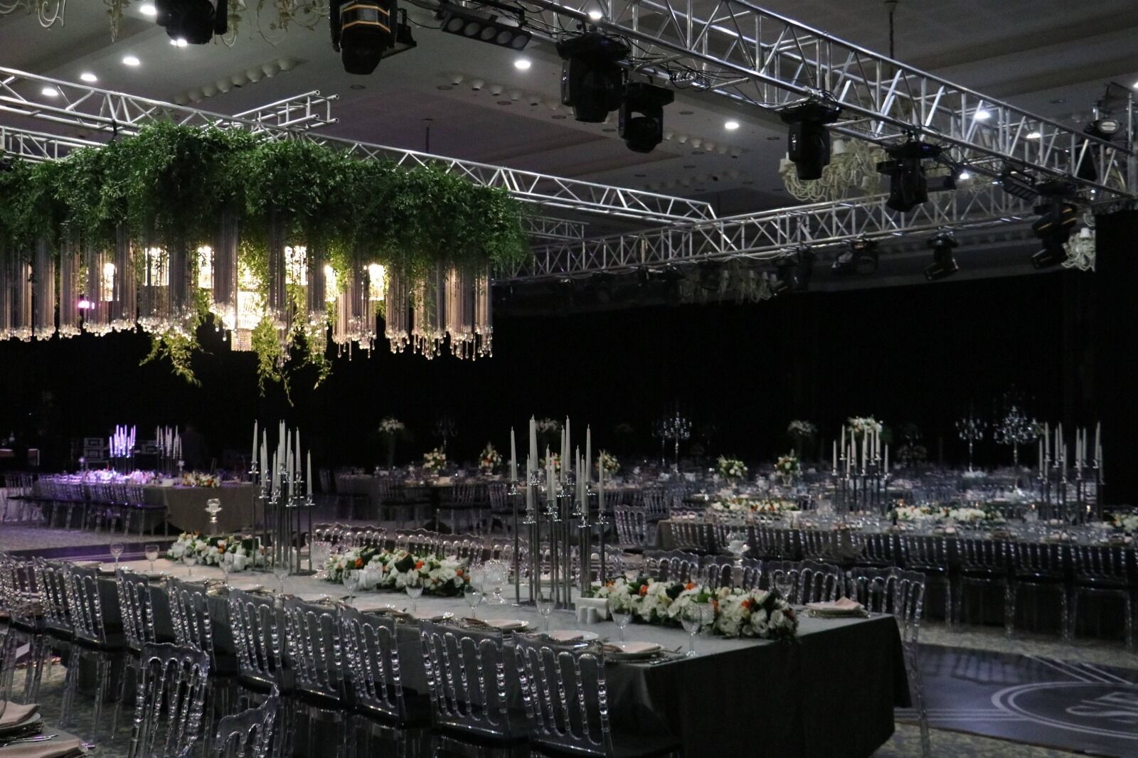 A banquet hall with multiple round tables set for dining, adorned with white flowers and candles.