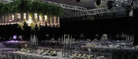 A banquet hall with multiple round tables set for dining, adorned with white flowers and candles.