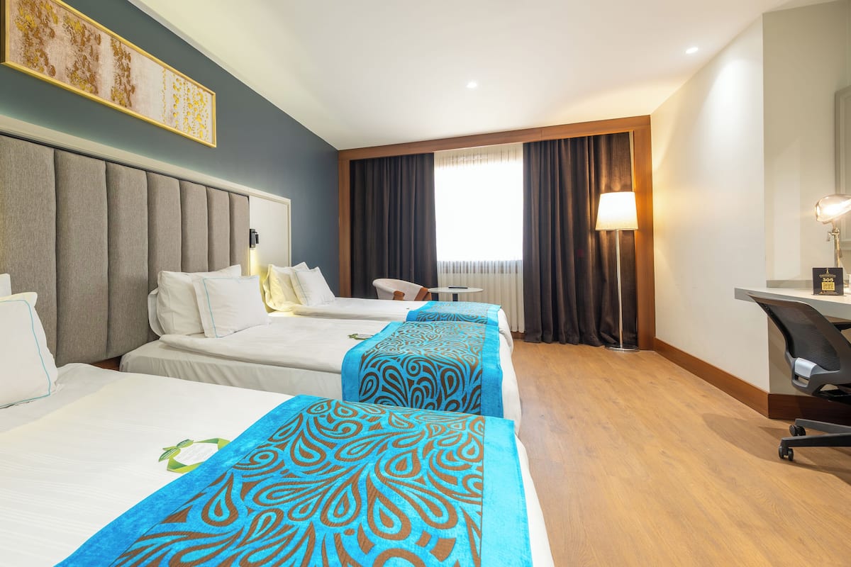 Habitación de hotel con dos camas, un escritorio, una silla y un ventanal con cortinas.