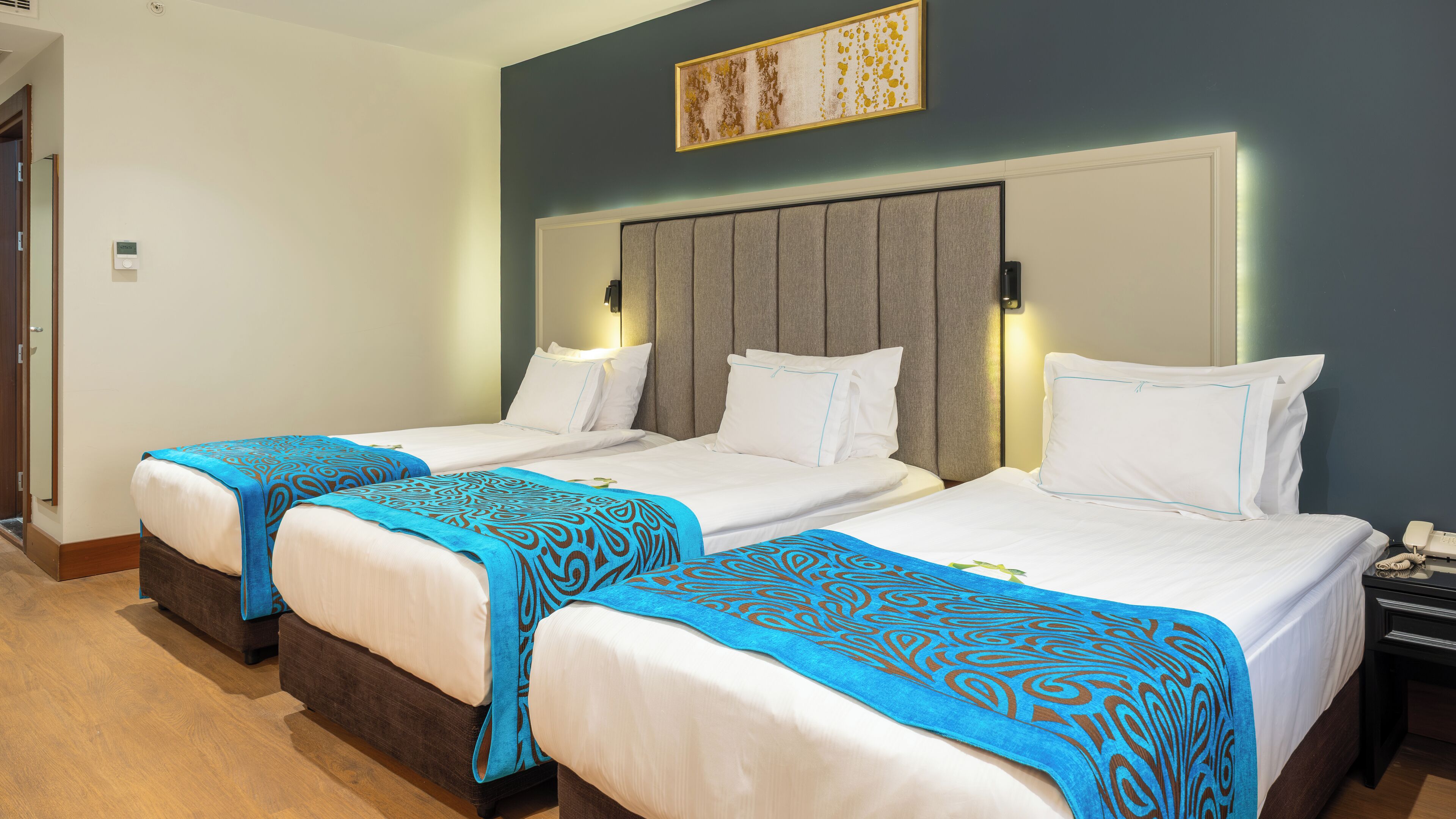 A hotel room with two beds, each with a blue patterned throw, white bedding, and a headboard with a light fixture.