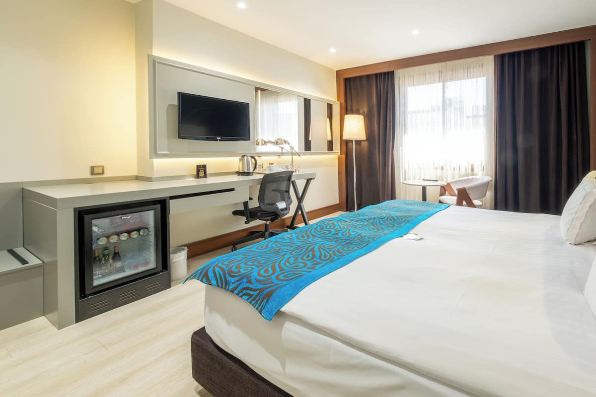 Habitación de hotel con cama, escritorio con computadora, minibar y televisión.