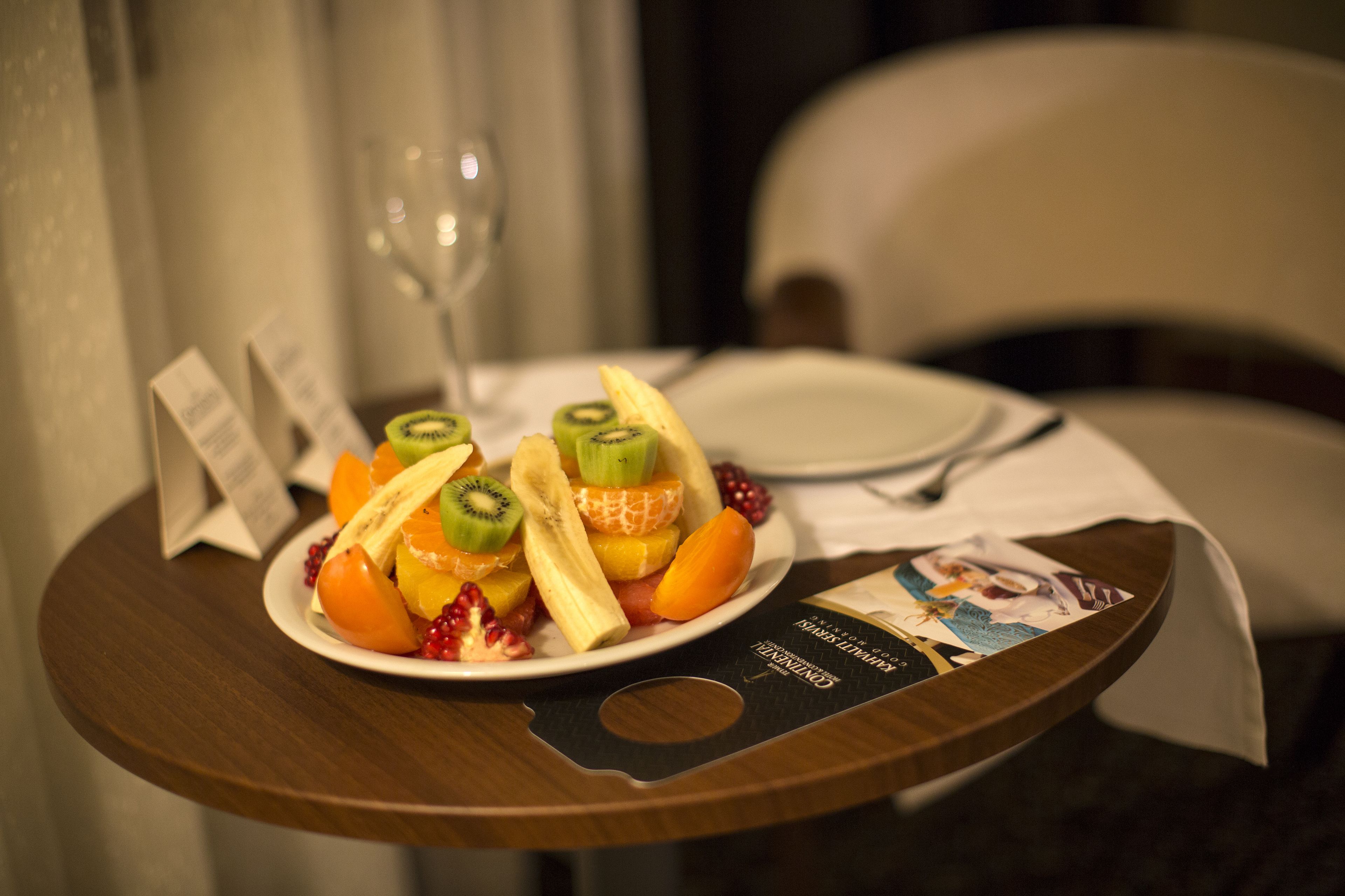 A fruit platter on a wooden table with a wine glass and a menu card.