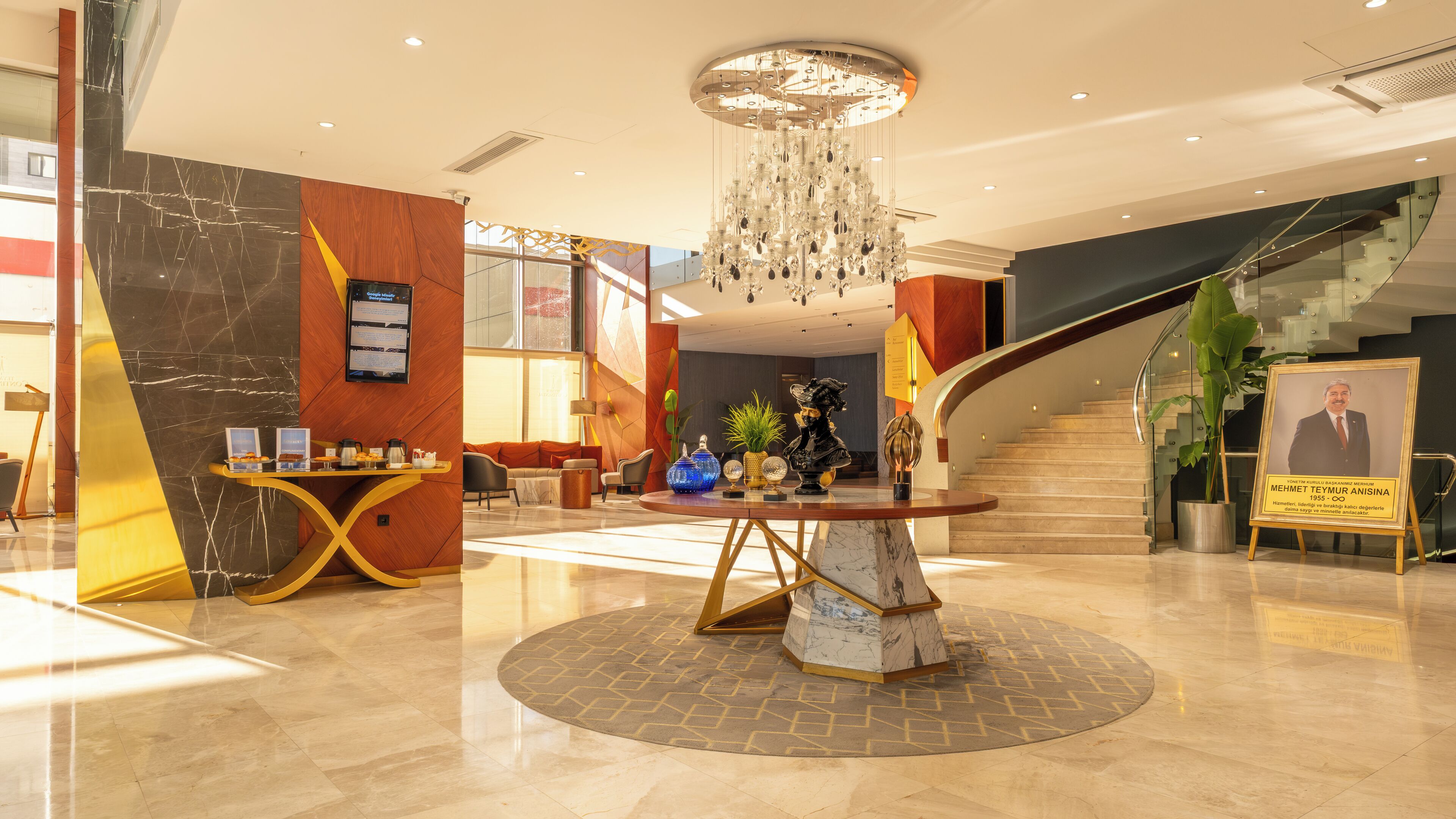 A modern lobby with a marble floor, a central round table, a staircase, and a chandelier.