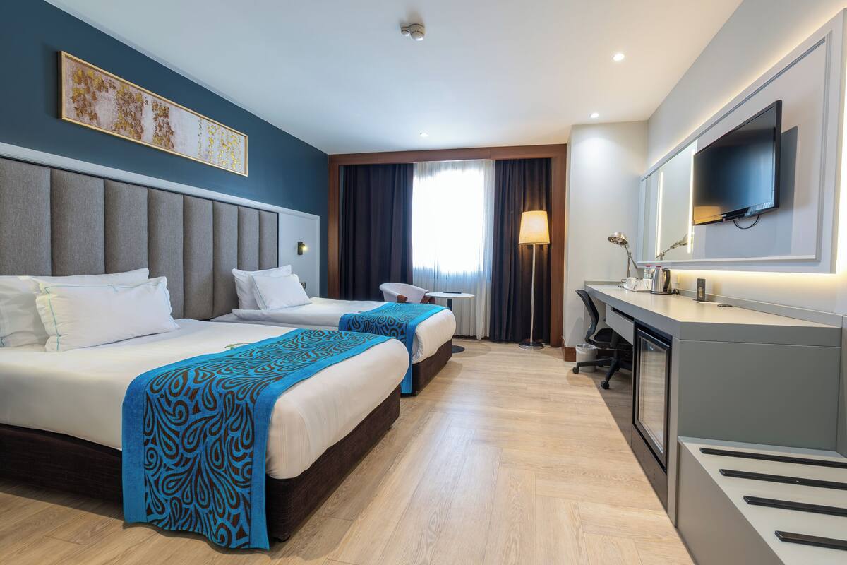 Habitación de hotel con dos camas, un escritorio, una silla, un televisor y una ventana con cortinas.