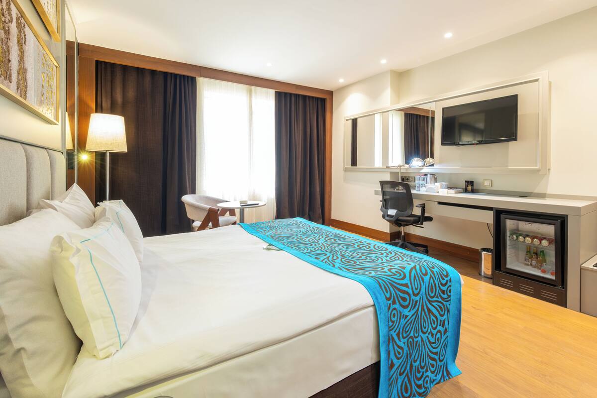 Habitación de hotel con cama, escritorio, silla, televisión y minibar.
