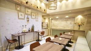 A restaurant with wooden tables and chairs, framed pictures on the walls, and a green cushioned bench. - Hotel The Bird (Amsterdam)