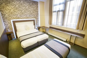 A hotel room with a large bed, a smaller bed, a window with curtains, a radiator, and a patterned wallpaper. - Hotel The Bird (Amsterdam)