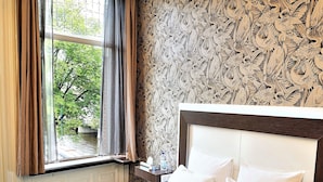 A hotel room with a large bed, a window with curtains, a patterned wallpaper, and a nightstand with a lamp. - Hotel The Bird (Amsterdam)