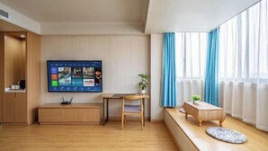 Un salon moderne avec un téléviseur à écran plat fixé au mur, un bureau en bois, une chaise, une petite table avec une plante et un banc agrémenté d’un tapis à motifs.