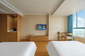 Hotelkamer met twee bedden, een televisie aan de muur, een bureau met stoel en een raam met uitzicht.