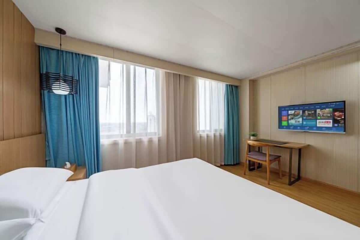 Una habitación de hotel con cama, escritorio, silla, televisión y cortinas.