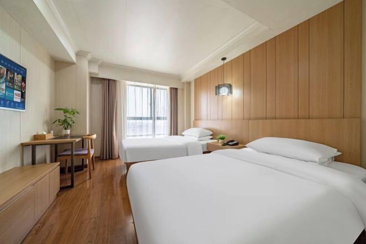 Habitación de hotel con dos camas, un escritorio, una silla, una planta y una ventana con cortinas.