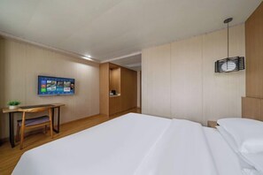 Een hotelkamer met een bed, een bureau, een stoel, een aan de muur bevestigde televisie en een hanglamp.