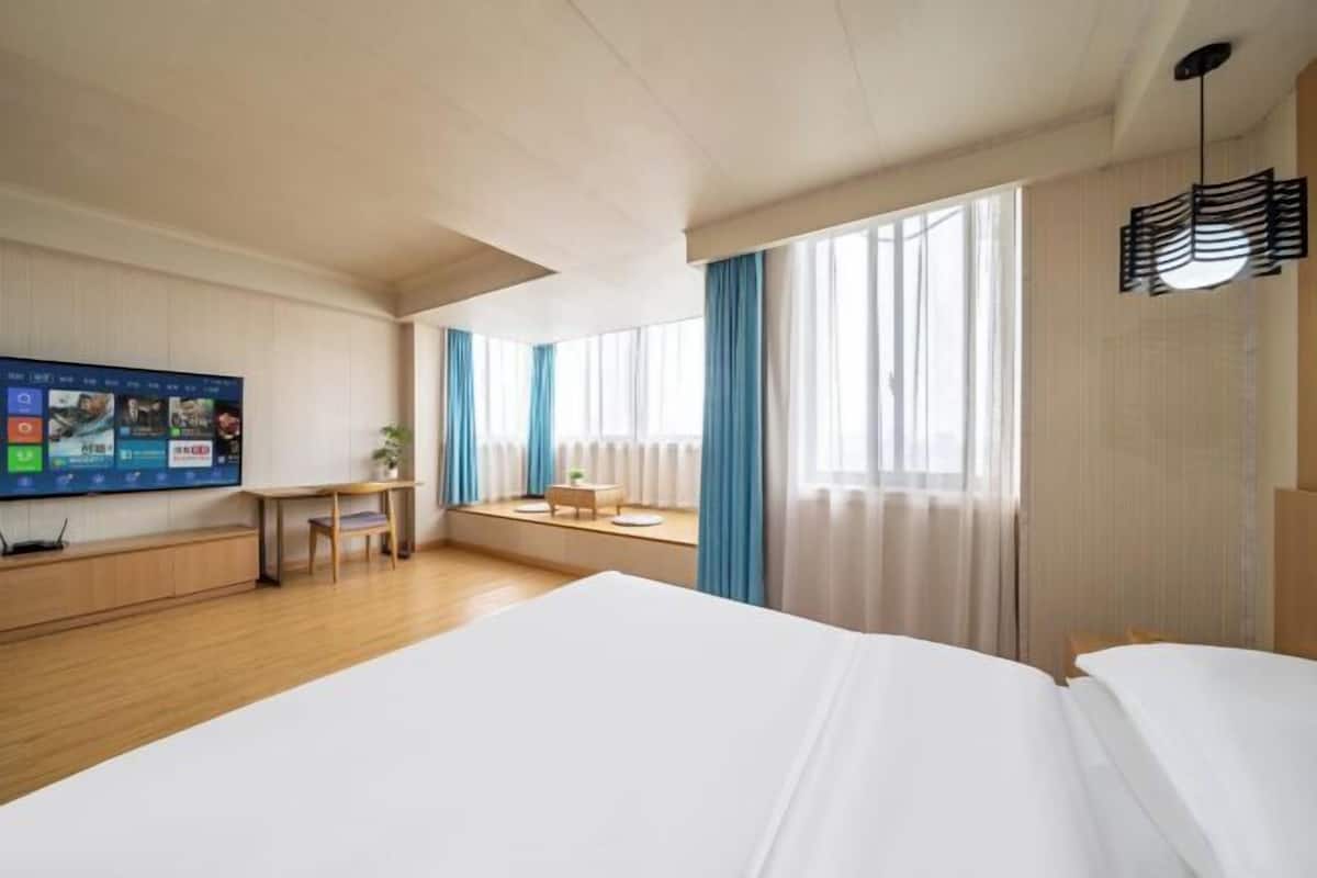 Una habitación de hotel con una cama grande, un escritorio, un televisor y una ventana con cortinas.