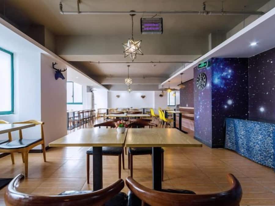 Uma ampla área de jantar com mesas e cadeiras altas, um mural de parede com tema de estrelas e um teto com luminárias pendentes.