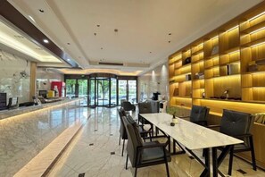 Eine Hotelhalle mit einer Marmor-Rezeption, einem langen Esstisch mit Stühlen und einer Wand mit beleuchteten Regalen.