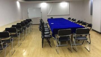 Un salón de conferencias con una larga mesa, sillas, una pizarra y una pantalla de proyector.