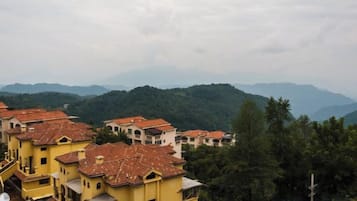 A residential area with yellow buildings and red-tiled roofs, surrounded by greenery and hills.