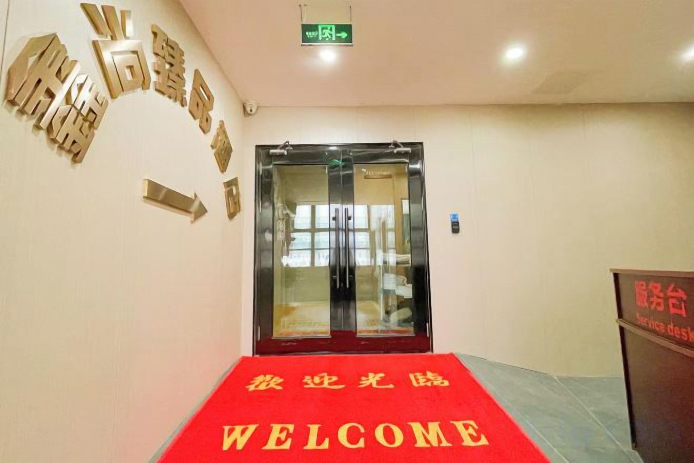 A hotel entrance with a red carpet, a glass door, and directional arrows on the wall.