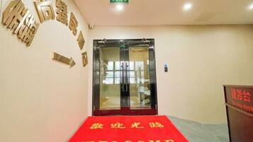 A hotel entrance with a red carpet, a glass door, and directional arrows on the wall.